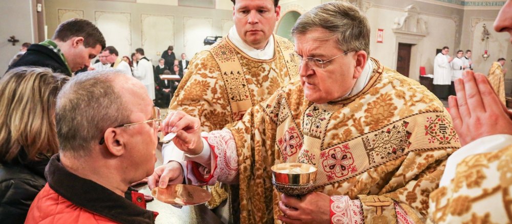 Kardinal Raymond Leo Burke teilt während der Eucharistiefeier die Mundkommunion aus