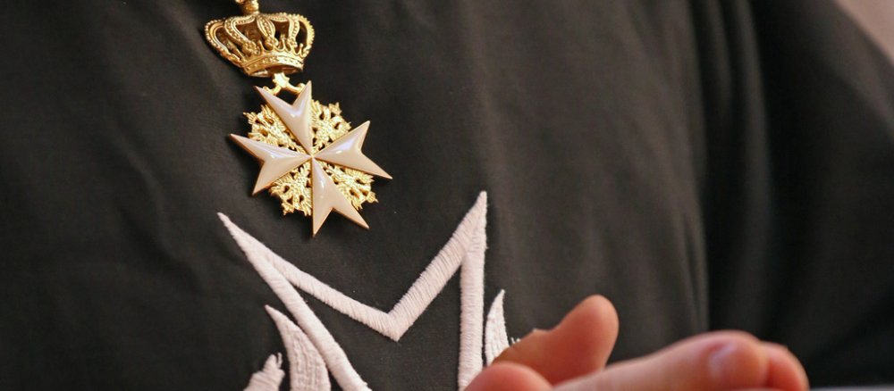 Praying hands in front of a Maltese cross