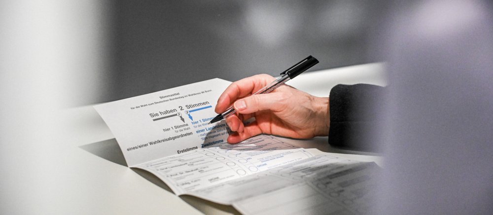 Eine Person füllt einen Stimmzettel aus in einer Wahlkabine