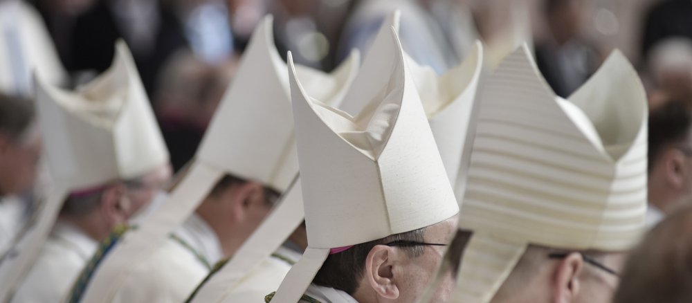 Bischöfe sitzen mit Mitren auf dem Kopf im Gottesdienst
