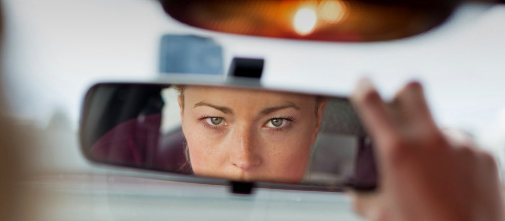 Eine Frau blickt in einem Auto in einen Rückspiegel.