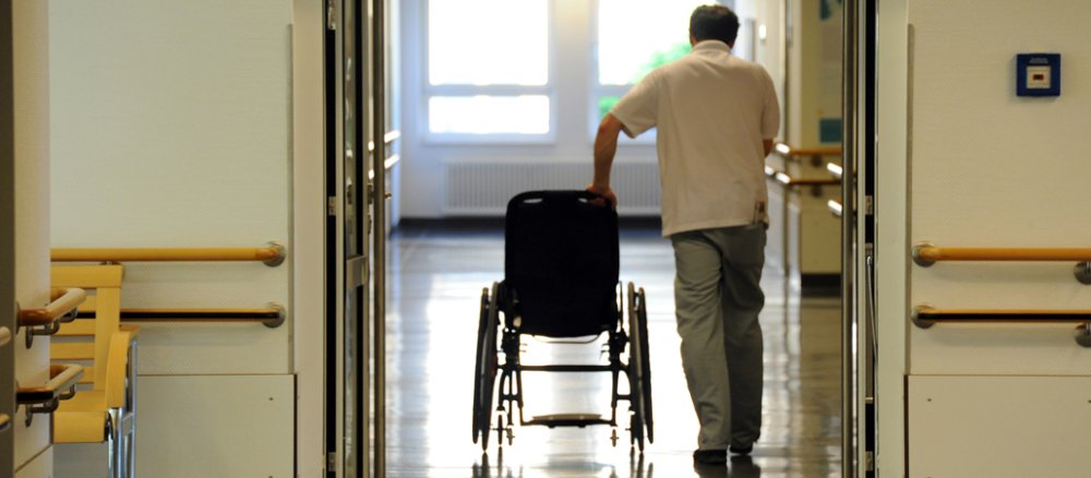 Ein Mann schiebt einen Rollstuhl durch ein Krankenhaus.