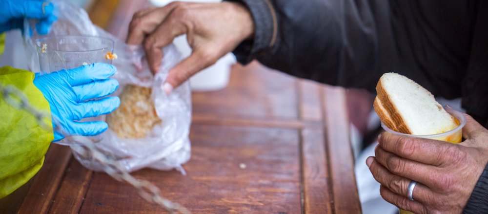 Ein Mann greift hält einen Becher mit Suppe in der Hand und greift in eine Tüte mit Brot