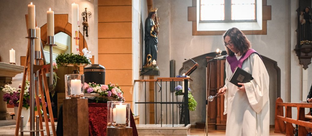 Eine Pastoralreferentin im weißen liturgischen Gewand mit violettem Kragen während einer Begräbnisfeier