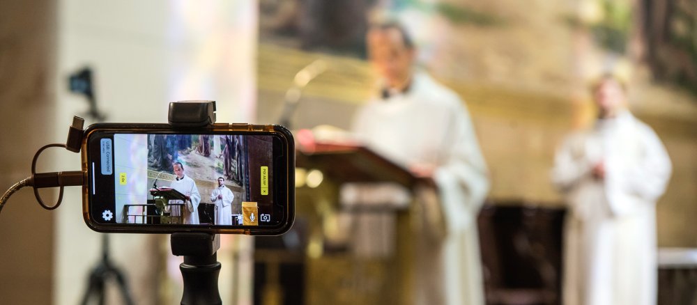Ein Smartphone filmt die Predigt eines Priesters am Ambo.