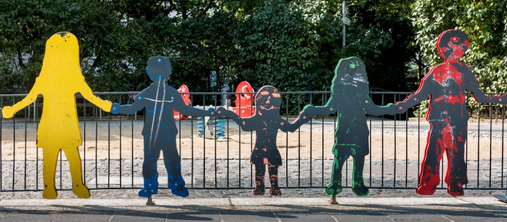 Holzfiguren in Lebensgröße stehen an einem Spielplatz.