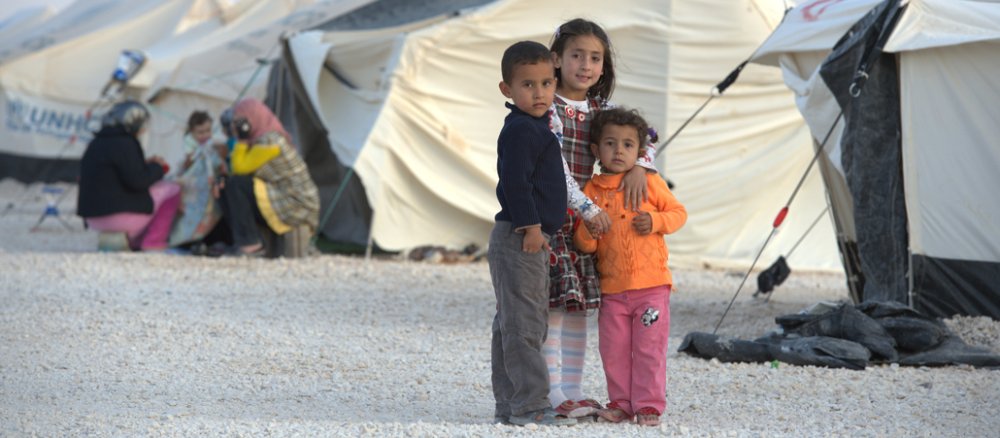 Drei Flüchtlingskinder vor einem Zeltcamp