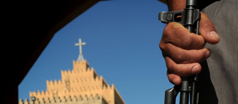 Ein Mann steht mit einer Waffe vor einer Kirche.