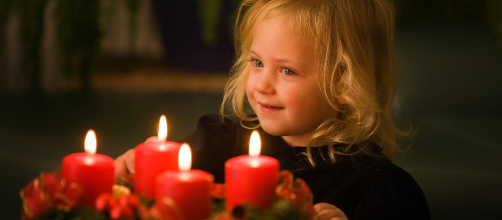 Ein Kind steht vor einem Adventskranz.