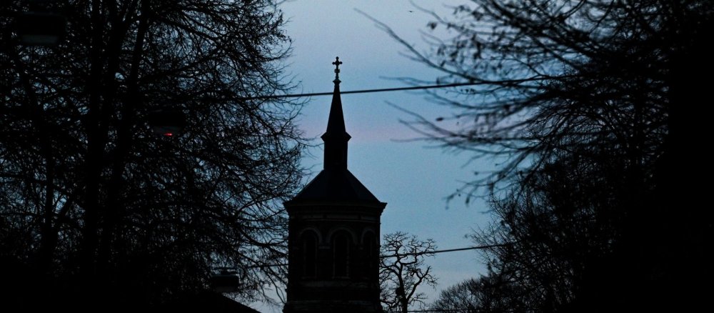Dunkler Kirchturm hinter Bäumen am Abend