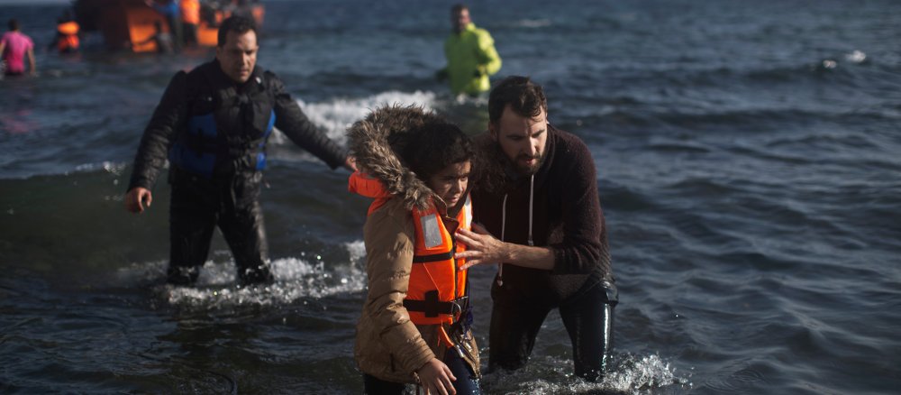 Ein Mädchen wird von einem Helfer von einem Flüchtlingsboot an den Strand gebracht.