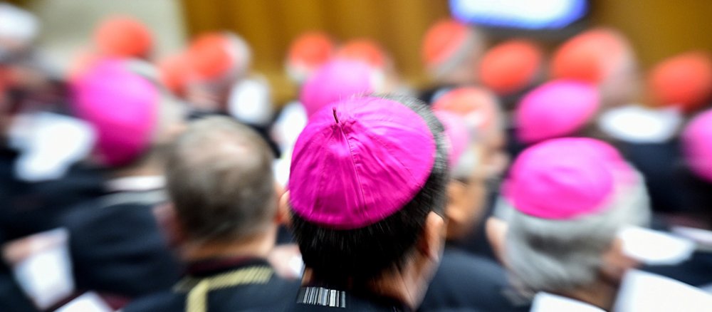 Ein Kopf mit Bischofsmütze wurde mit der Kamera schnell anvisiert, alle anderen Kopfbedeckungen von Bischöfen und Kardinälen sind verschwommen im Bild.