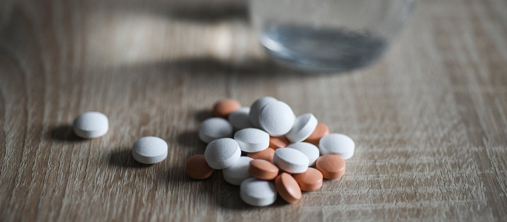 Viele Tabletten liegen neben einem Wasserglas auf einem Holztisch