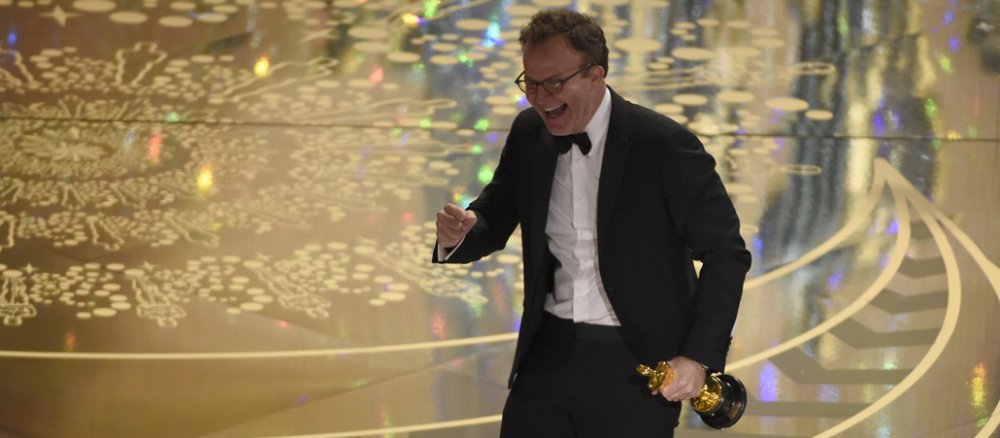 Ein Mann mit einer Trophäe in der Hand geht über eine Bühne.