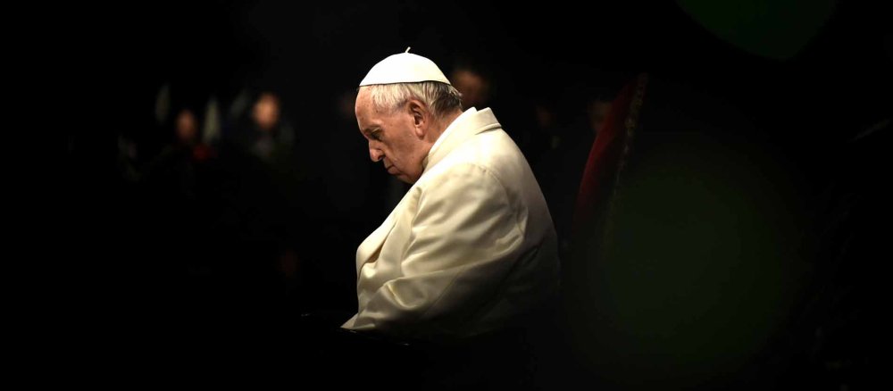 Pope Francis lowers his head, everything around him is dark