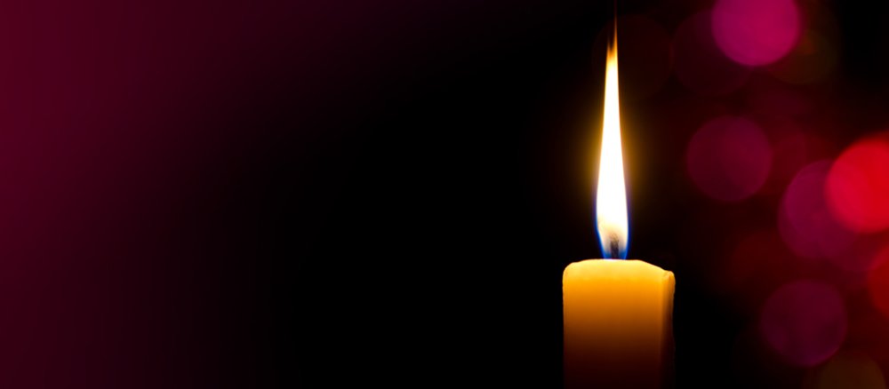 Kerze leuchtet alleine vor verschwommenen Hintergrundlichtern