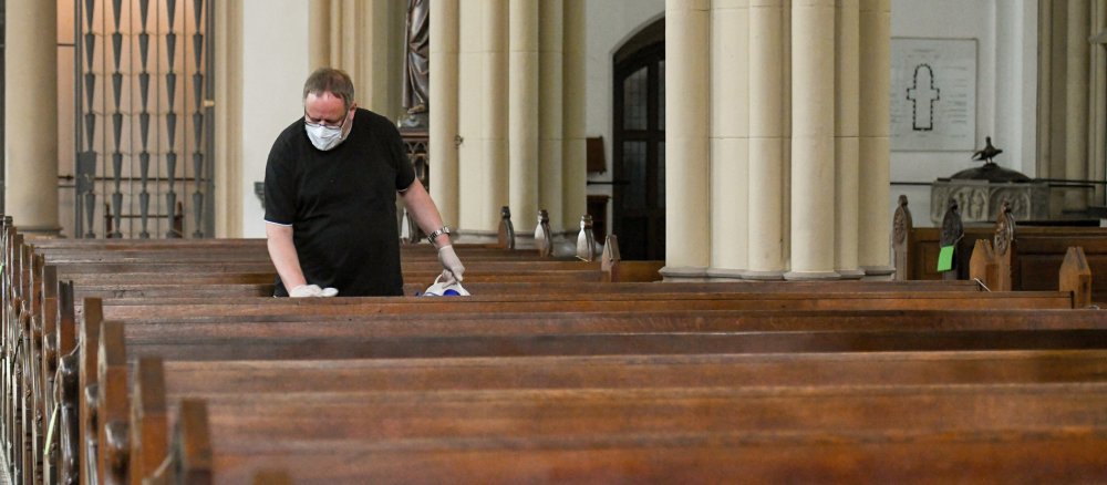 Ein Küster desinfiziert ein Kirchenbank