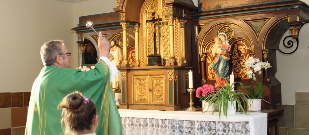 Ein Pfarrer segnet zwei Heiligenfiguren auf einem Altar.