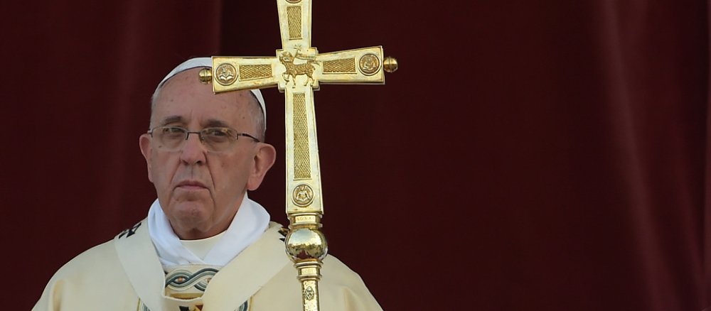 Papst Franziskus blickt ernst, er hält ein Kreuz in der Hand.