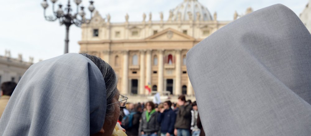 Two nuns with veils in St Peter's Square look towards St Peter's Basilica.