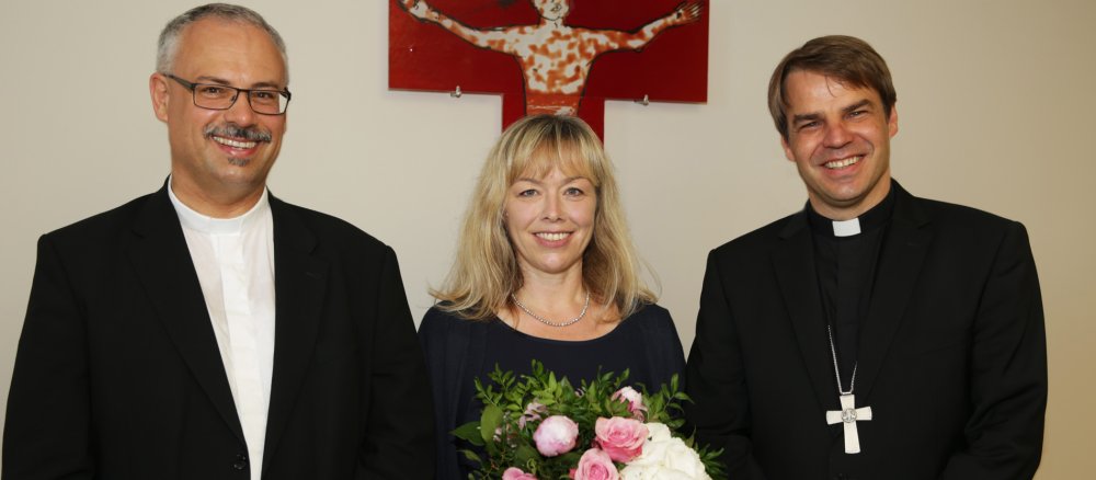Der Generalvikar von Passau, Klaus Metzl, Antonia Murr, Kanzlerin der Diözese Passau und Bischof Stefan Oster stehen vor einem Kreuz.