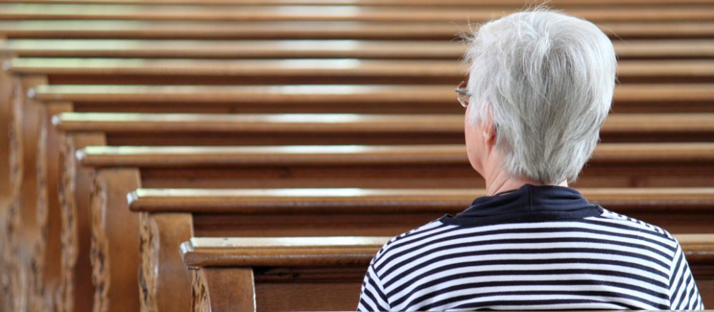 Eine ältere Frau sitzt alleine in der Kirchenbank