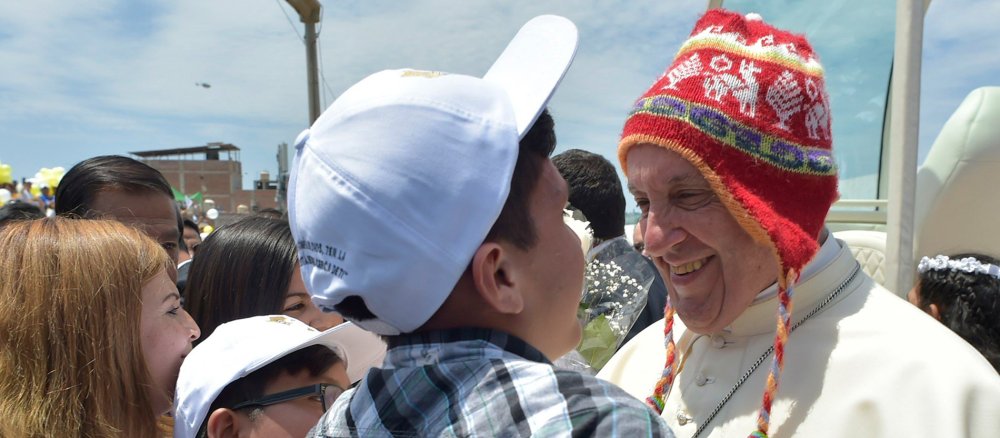 Papst Franziskus trägt eine rote Mütze und lacht einen Jungen an, beim Besuch des Viertels Buenos Aires am 20. Januar 2018 in Trujillo (Peru).