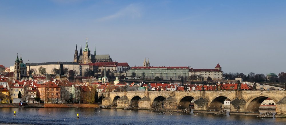Blick vom Wasser auf eine Brücke, dahinter liegt ein bebauter Berg mit einer großen Kirche.