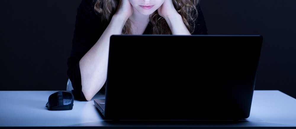 Eine junge Frau sitzt am Laptop und stützt ihren Hals mit den Händen ab. Sie sieht besorgt aus.
