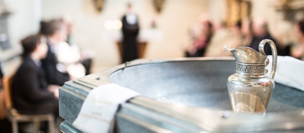 Ein Taufbecken in einer Kirche, im Hintergrund die Gemeinde