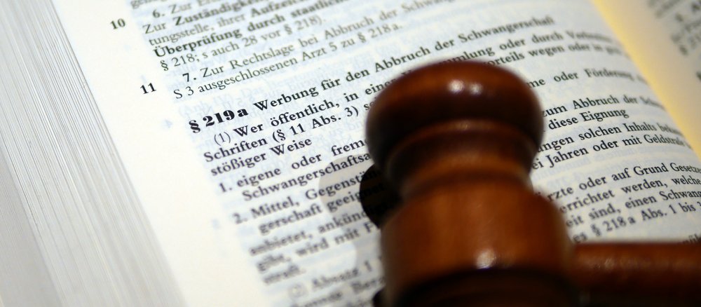 Ein Richterhammer liegt auf einem bei § 219a aufgeschlagenen StGB-Kommentar