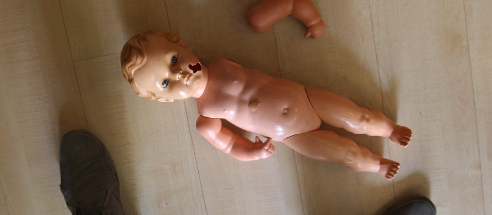 Eine beschädigte Kinderpuppe liegt auf dem Boden