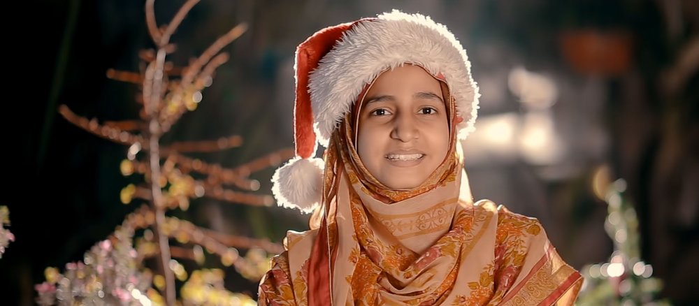 Eine pakistanische Frau trägt eine Weihnachtsmannmütze auf dem Kopftuch.