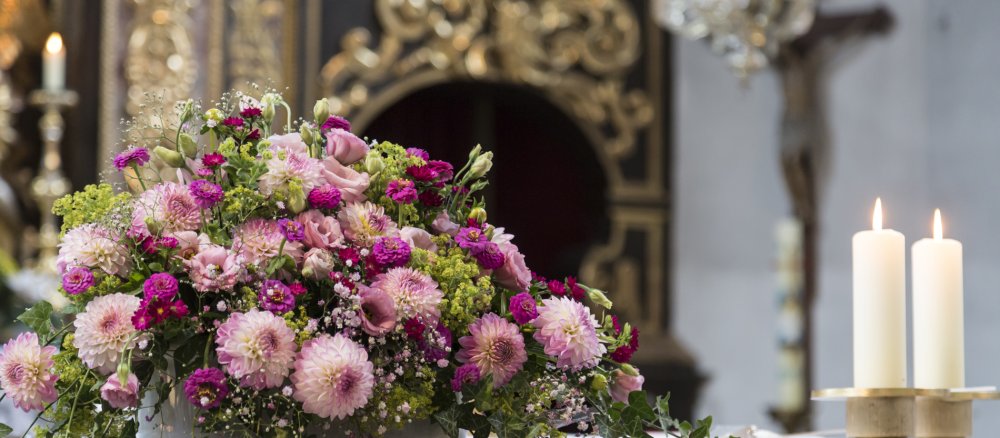 Ein Blumengesteck steht in einer Kirche auf dem Altar neben zwei Kerzen.