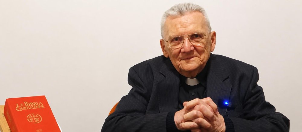 Don Lanfranco Casali sitzt neben einer Bibel, die Hände gefaltet