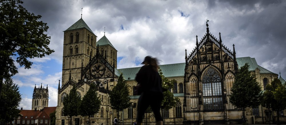 Dunkle Wolken über dem Paulusdom in Münster. Eine Passantin geht über den Platz.