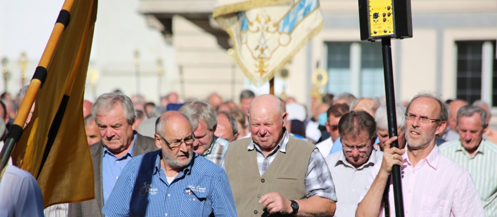 Männer tragen bei einer Wallfahrt Flaggen und Wappen.