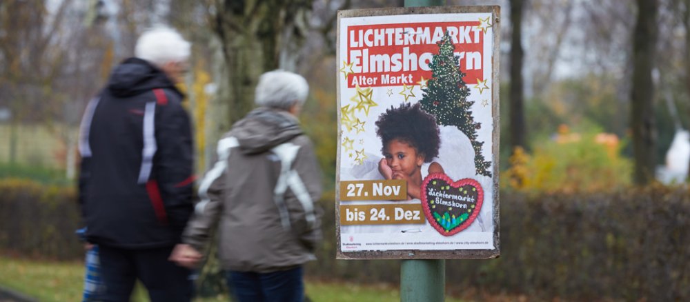 Plakat mit der Aufschrift "Lichtermarkt Elmshorn - Alter Markt - 27. Nov bis 24. Dez" zeigt ein dunkelhäutiges Mädchen als Engel.