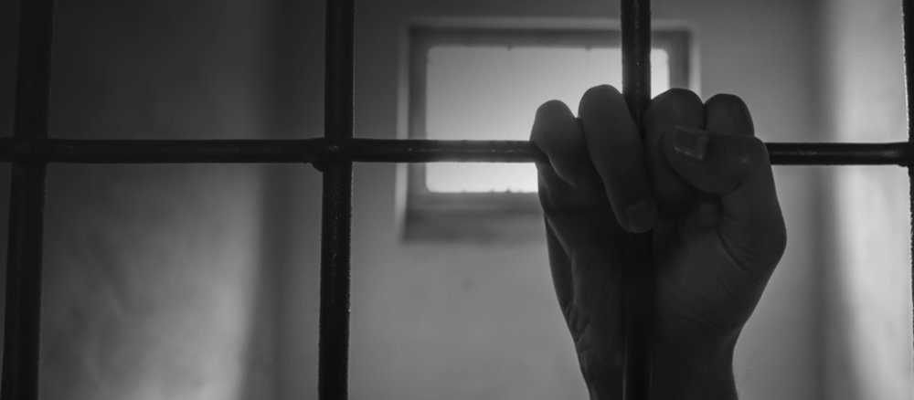 Schwarzweißbild, Hand krallt sich an Gefängnisgitter