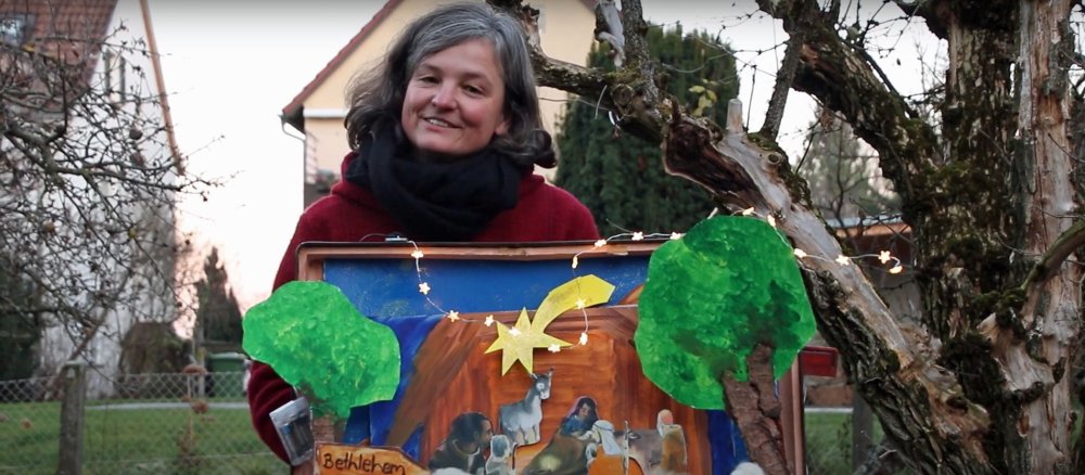 Claudia Ebert steht in einem Garten hinter einem geöffneten Reisekoffer