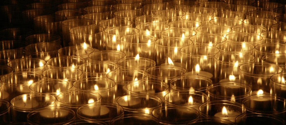Opferlichter stehen dicht aneinander im Dunkel einer Kirche.