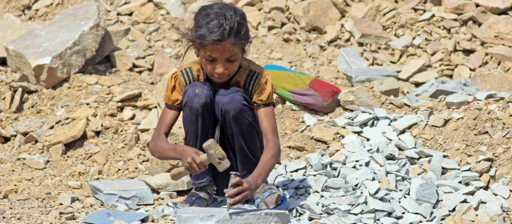Die etwa 8-jährige Sunita sitzt in Kota, in der indischen Provinz Rajasthan, in einem Steinbruch und arbeitet mit Hammer und Meißel.