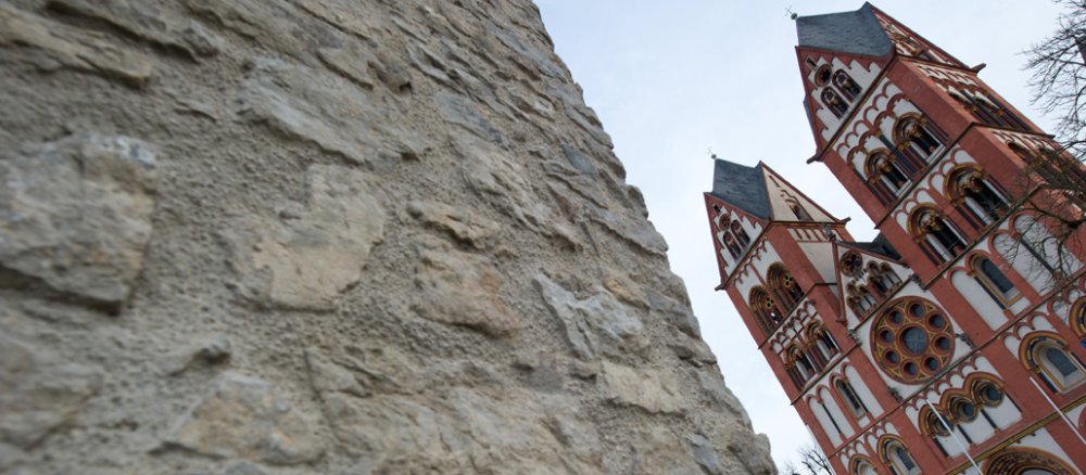 Links im Bild eine große Mauer, rechts der Limburger Dom.