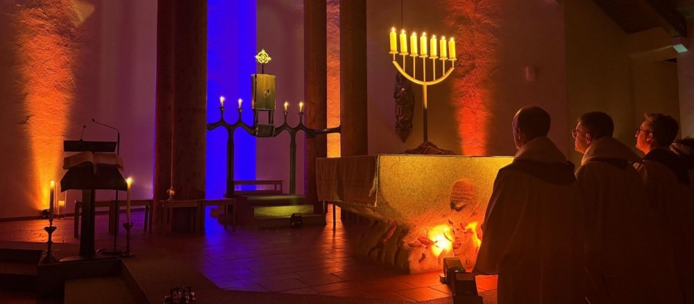 Drei Personen stehen im Altarraum der dunklen Kirche.