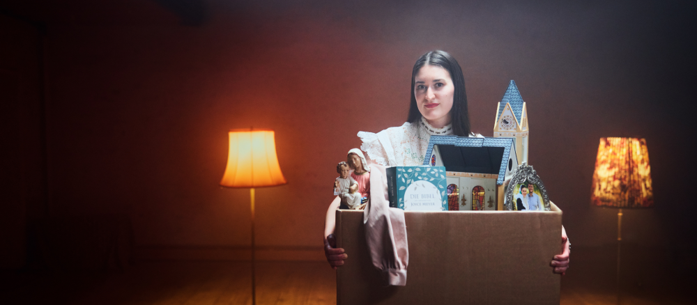 Gloria hält einen Karton mit Kirche und Bibel