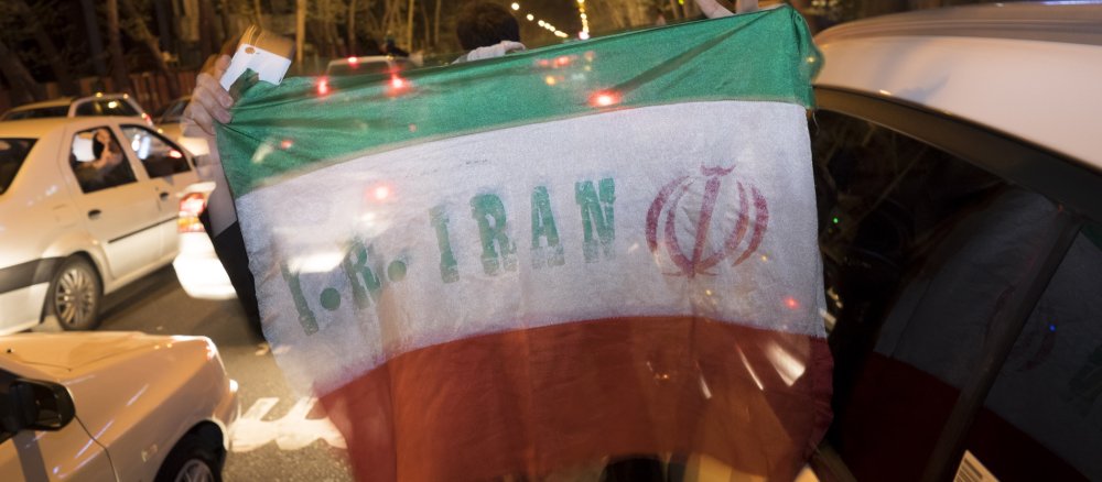 Ein Mann hält auf einer Straße eine iranische Flagge hoch