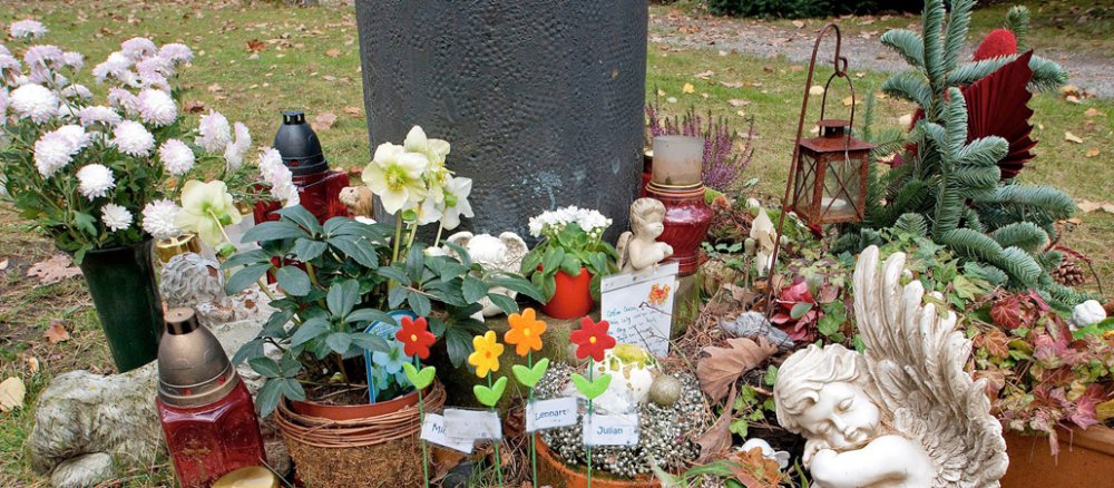 Blumen, Briefe und Grablichter auf einem Kindergrab.