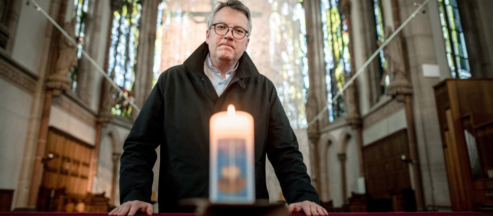 Pfarrer Christoph Wichmann steht hinter einer brennenden Kerze in einer Kirche