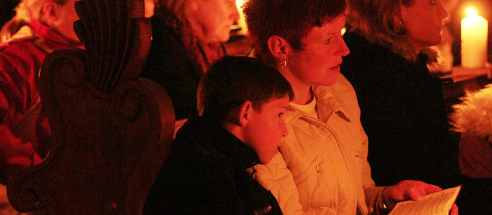Ein Junge lehnt sich an seine Mutter im kerzenbeschienenen Kirchenraum