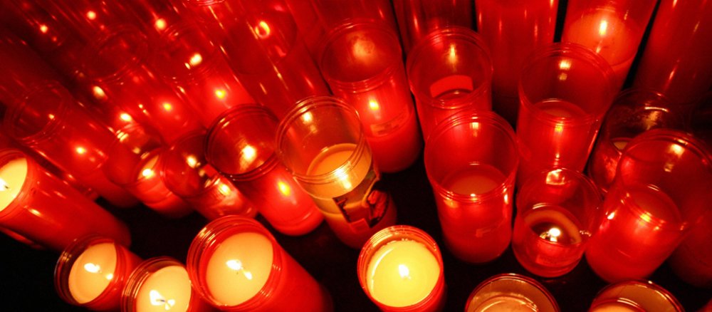 Kerzen brennen in roten Plastikbehältern in einer Kirche.